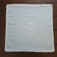 Pearl Embellished Challah Cover, 18” x 18” shown with petite pearl border and embroidered center design in pearl-colored thread. The understated, soft-white embroidery spells out Shabbat v’Yom Tov in Hebrew lettering, encircled by a leafy wreath design.