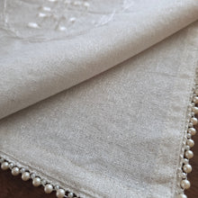 Closeup corner detail of the Pearl Embelllished Challah Cover in a natural white woven fabric background with subtle silver flecks. Enlargement shows the smaller and larger alternating pearl beads trimming the outside edges.