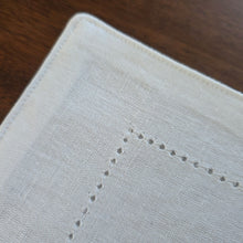 Enlarged corner detail of a white, woven challah cover, showing the decorative, keyhole hem-stitchng.